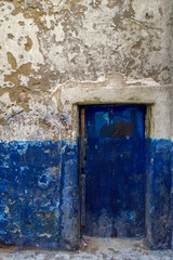 An old, run down blue and white painted doorway with flecked, worn paint texture in the medina of Essaouira on Morocco's Atlantic coast