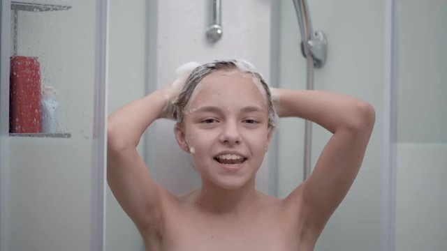 Smiling young girl bathing under a shower at home. Beautiful teen girl taking shower and washing in the bathroom. Happy child washing head, face and body with water.