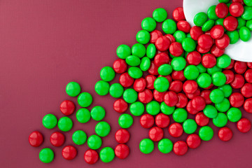 Red and green Christmas candy spilling out of a white bowl onto a red background
