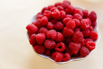 Red fresh raspberries in white bowl on light rustic wood background. Top view with copy space. Selective focus. Vegetarianism