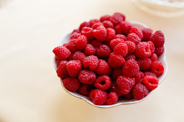 Red fresh raspberries in white bowl on light rustic wood background. Top view with copy space. Selective focus. Vegetarianism