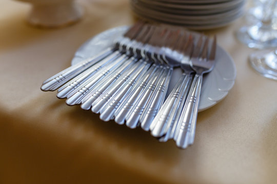 Clean Cutlery: Forks In White Plates And A Blurred Stack Of Plates In The Background Stand On A Wooden Shelf