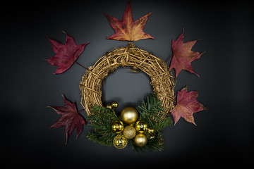 Twig Christmas wreath with golden balls and red dried leaves on black.