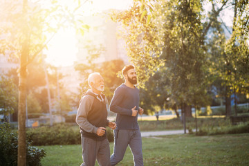 Happy father and son jogging together outdoors in park.