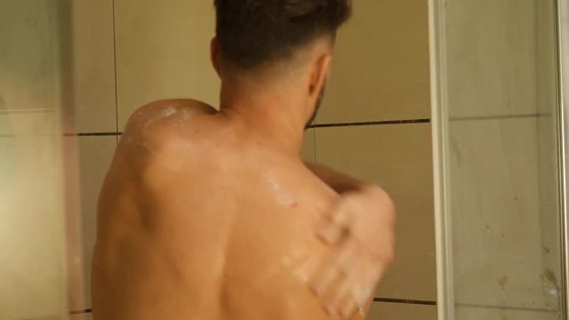 Close up of Back of Young Bare Muscular Young Man Taking Shower, Looking Down