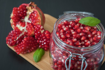 Delicious pomegranate seeds placed in glass jar with fresh organic pomegranates on rustic wooden background.Close up,Copy space