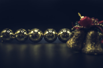 Desaturated golden Christmas balls and bells on black background.