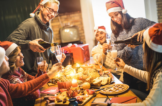 Friends group with santa hats celebrating Christmas with champagne and sweets food at home dinner - Winter holidays concept with people enjoying time and having fun eating together - Warm filter