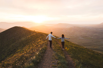Young couple running together by sunset hill with amazing mountain view