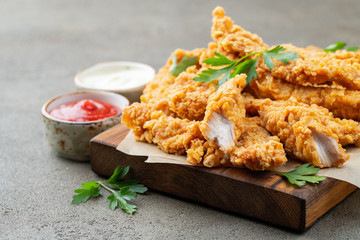 Breaded chicken strips with two kinds of sauces on a wooden Board. Fast food on dark brown...