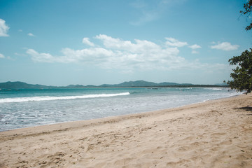 Fototapeta na wymiar Empty sandy beach of Tamarindo with turquoise waves and mountains around the bay