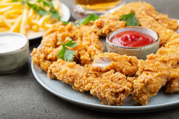 Breaded chicken strips with tomato ketchup on a white plate. Fast food on dark brown background