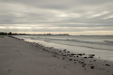 View of Fort Meyers in background during sunrise along beachfront on stormy morning along Fort Myers Beach on Estero Island in Florida. 