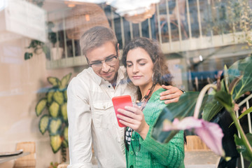 Hugging wife. Loving caring man wearing glasses hugging his beautiful wife showing him some photos