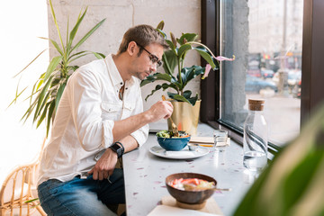 Vegan cafe. Stylish handsome man wearing white shirt feeling relaxed while eating lunch in vegan cafe