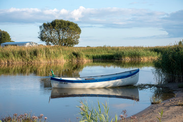 Obraz premium Lonely boat in tranquil rushy backwater lit by evening sun