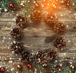 Old wooden Christmas background. Fir branches with baubles and gold stars. Cones in the shape of a circle. Space for Xmas congratulation text. Top view. Effect of snow and light.