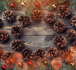 Fototapeta na wymiar Old wooden Christmas background. Fir branches with baubles and gold stars. Cones in the shape of a circle. Top view. Space for Xmas congratulation text. Light effect.