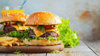 Two fresh homemade burgers with fried potatoes and orange juice on a wooden table. With copy space