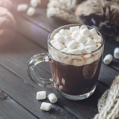 Hot cocoa with marshmallows in a glass cup surrounded by Christmas gifts and winter clothes, Christmas atmosphere and coziness