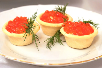 On a plate are three tartlets with red caviar. Delicious festive delicacy for the new year, Thanksgiving or other dinner. Registration of dishes in a cafe or restaurant.