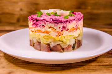 White plate with russian traditional new year salad herring under fur coat on wooden table