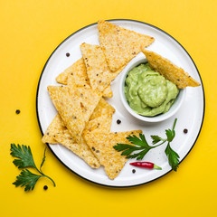 Traditional Mexican Guacamole With Corn Chips Nachos on yellow background