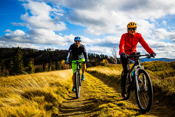 Fototapeta premium Cycling woman and man at Beskidy mountains autumn forest landscape. Couple riding MTB enduro track. Outdoor sport activity.