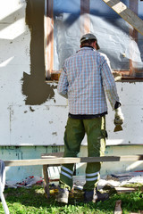 Man holding trowel applying construction glue layer on insulated wall for covering fiberglass reinforcing mesh on rigid polyurethane foam sheets around window. DIY home improvement insulation concept.