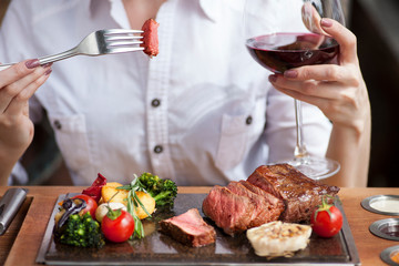 Woman eating steak and drinking a wine