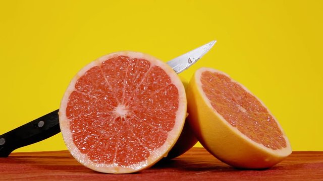Ripe pomelo fruits (exotic variety of the Citrus familiy), full and halved, with a sharp knife, on a rotating surface. Medium close-up shot.
