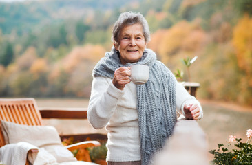 An elderly woman sitting outdoors on a terrace in on a sunny day in autumn.