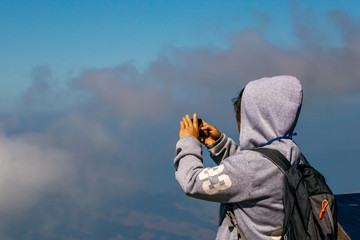 Fototapeta premium The Asian woman with backpack is looking and taking photo to the view of the mountain or nature background from the balcony in Thailand. 