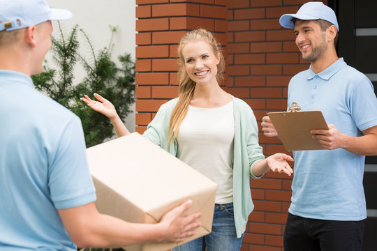 Happy woman welcoming professional couriers with package and receipt of delivery