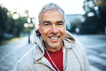 A portrait of an active mature man standing outdoors in city, wearing hoodie.