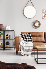 Vertical view of warm ethno living room with leather couch with patterned pillow and mirror and clock on beige wall, real photo