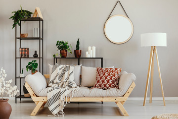 Green plants in pots, candles and books on metal shelves in beige scandinavian living room with comfortable settee, lamp and mirror on the wall - obrazy, fototapety, plakaty