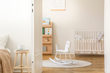 Scandinavian nursery with white wooden crib, round carpet and rocking horse in the middle, real...