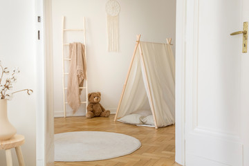 Stylish kids playroom with white tent, teddy bear, macrame on the wall and round carpet on the...