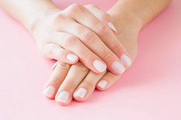 Young, perfect woman's hands with light nails on pastel pink table. Care about clean, soft and smooth skin. Manicure, pedicure beauty salon.