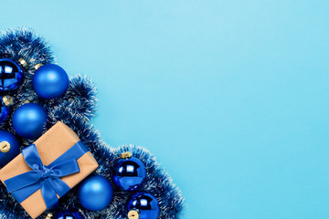 Gift box with blue ribbon, blue Christmas tree toys, balls on a blue background. Concept of Merry Christmas and Happy New Year. Flat lay, top view
