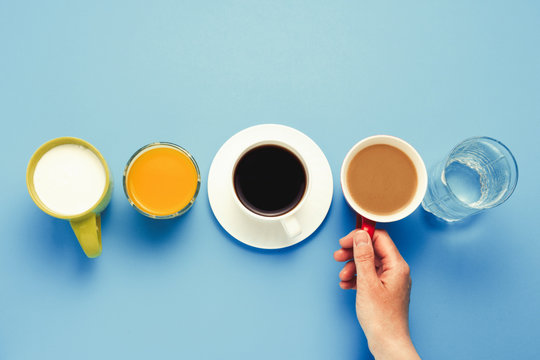 Woman's hand takes a cup with coffee with milk Group of healthy drinks, orange juice, coffee, water, yogurt on a blue background. Flat Lay Still Life Table Top View