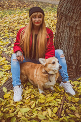 Naklejka na ściany i meble Woman with Red dog of Corgi breed for a walk in the city streets. The life of dogs in cities. Dog lover with her pet 