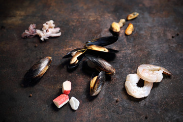 Frutti di mare  krewetki, małże, ośmiorniczki, ślimaki, paluszki krabowe. Składniki potrawy na ciemnym tle. © foodandcook