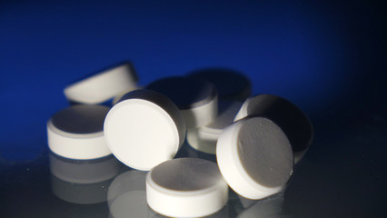 A bunch of white round pills on the table. On a blue background. Close up.