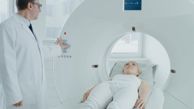 In Medical Laboratory Radiologist Controls MRI or CT or PET Scan with Female Patient Undergoing Procedure. High-Tech Modern Medical Equipment. Camera Zooms in on a Patient.