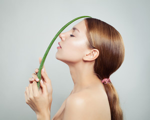 Beautiful woman with healthy hair and clear skin holding green aloe leaf