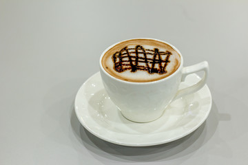 The white cup of hot capuchino and chocolate syrup on top on the wooden table background.