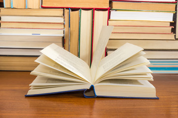 Open book on wooden table against background of other books
