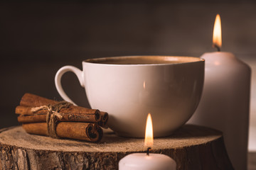white cup with coffee, cinnamon and candles 